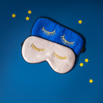 Two playful sleep masks with eyelash design on blue background with star accents