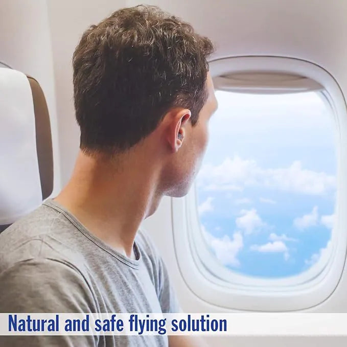 Man sitting on an airplane seat, looking out the window at clouds, wearing a small earplug for pressure relief.