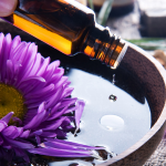 Essential oil dripping into a bowl of water with a purple flower